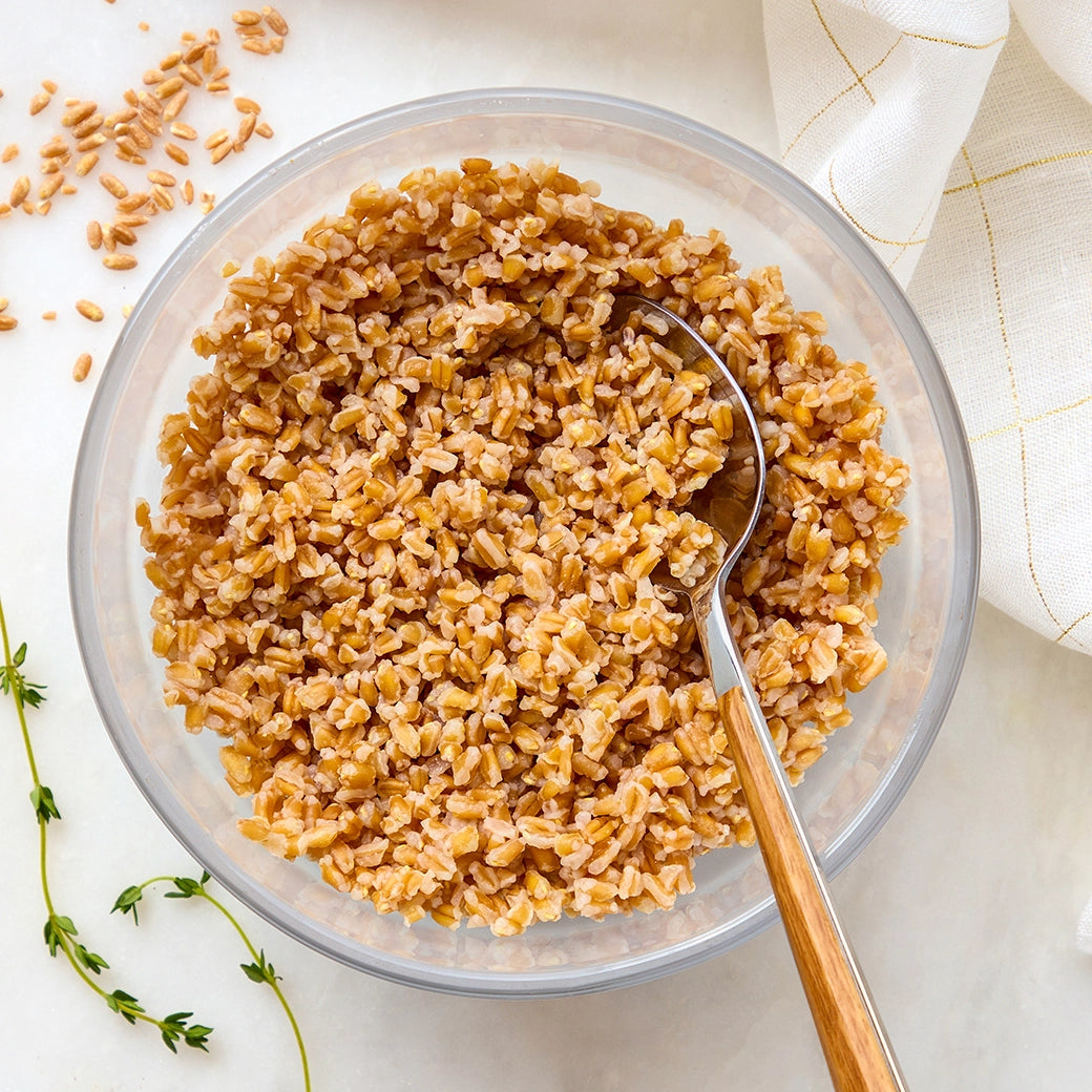 Cooked farro grains in a clear Anyday dish with a spoon and lid nearby