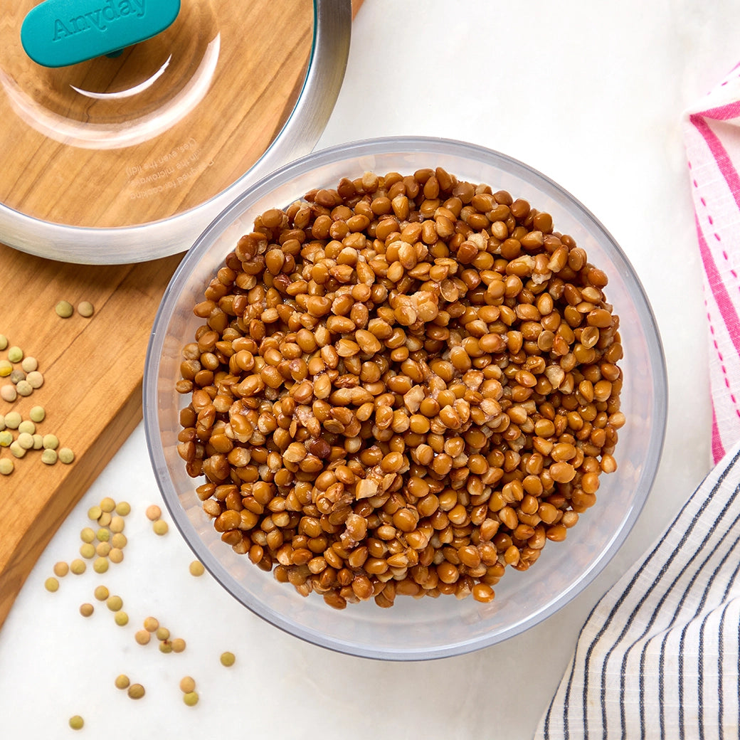 Cooked brown lentils in a clear Anyday dish with a spoon and lid on a light surface