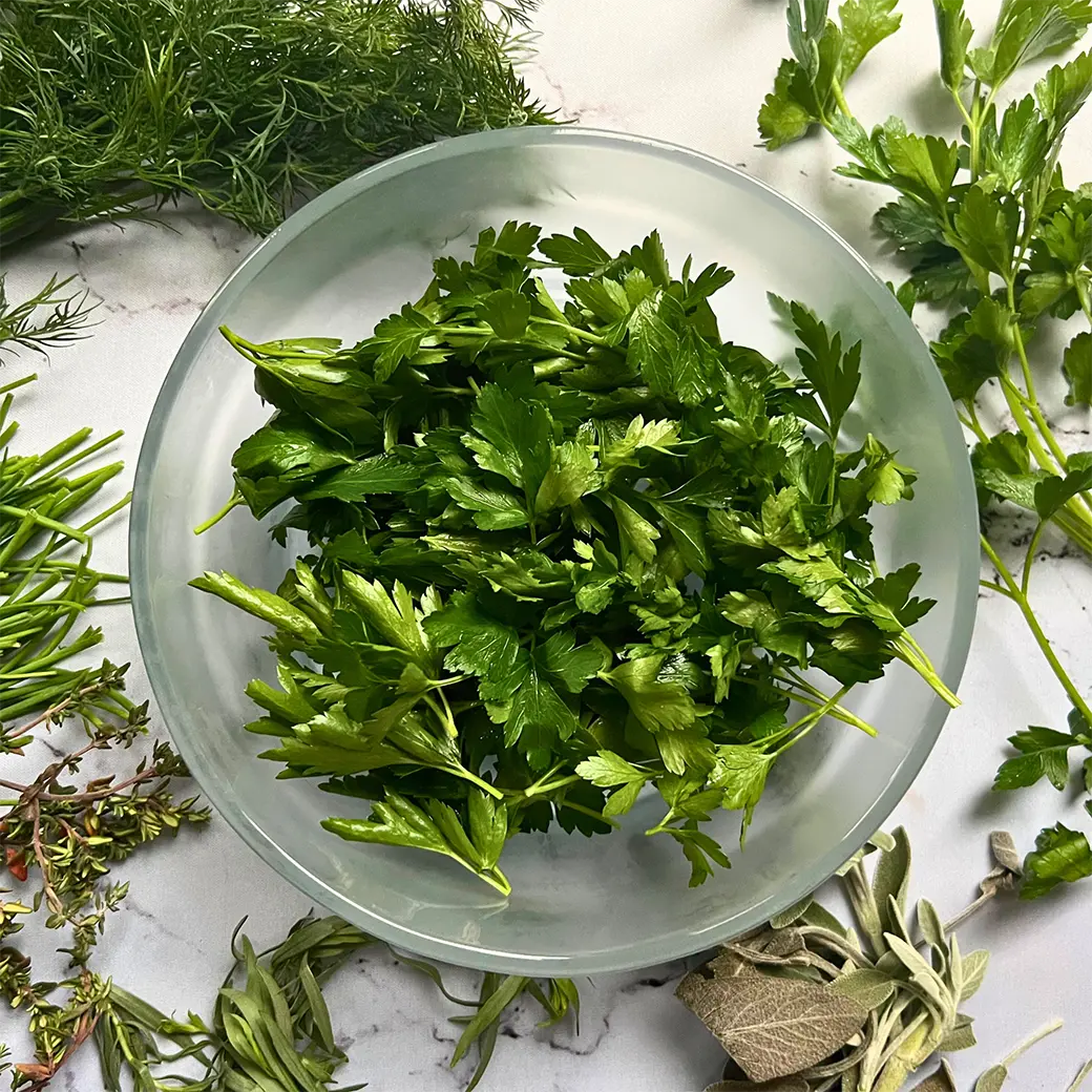 Dried herb leaves in a clear Anyday dish after microwave drying, on a neutral background