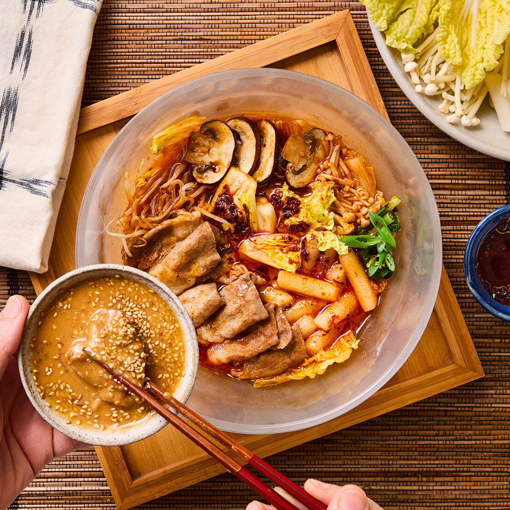 An Anyday dish filled with hot pot ingredients, including thinly sliced beef, rice cakes, mushrooms, and Napa cabbage in a rich, spiced broth.