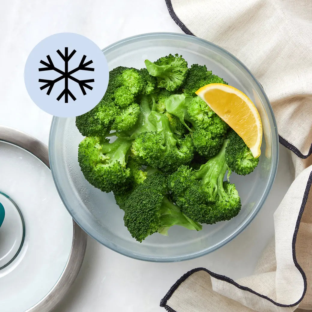 Frozen broccoli florets in a clear Anyday dish with visible steam and lid nearby