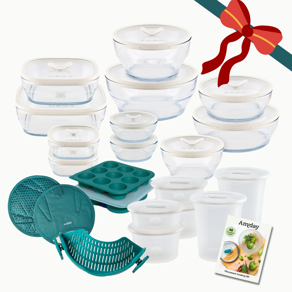 The Everything but the Microwave Bundle (mochi) featuring glass storage dishes, silicone baking molds, a silicone steamer basket, and a recipe book, all tied with a red decorative ribbon.