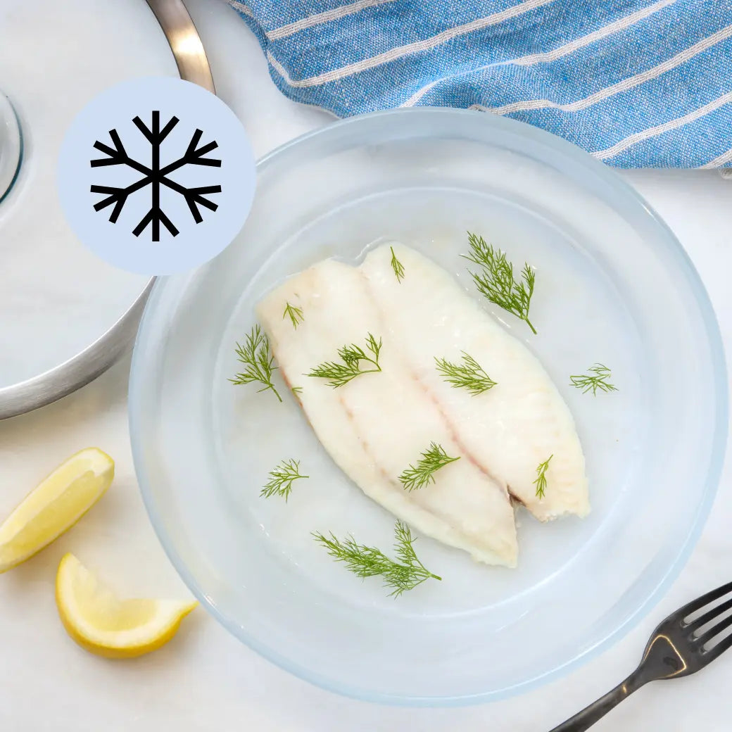 Frozen tilapia fillet in a clear Anyday dish with lid off to the side on a neutral surface