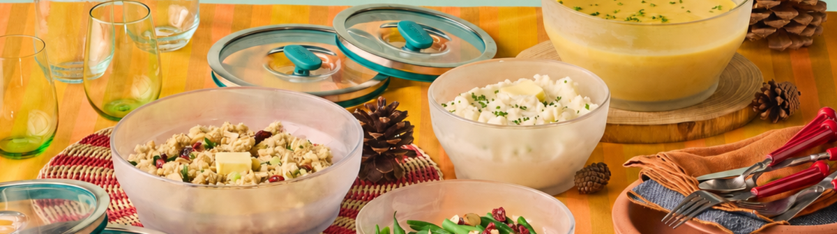 A spread of various prepared dishes in glass bowls, including stuffing, mashed potatoes, green beans, and soup, on a table set with pinecones and cutlery.
