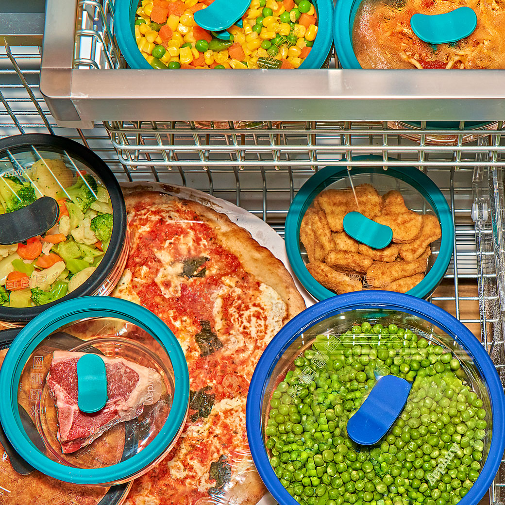 A freezer drawer packed with clear Anyday dishes containing frozen vegetables, soup, pizza, and a steak, sealed with silicone-rimmed lids.