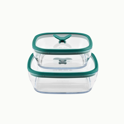 Two frosted glass Anyday 4-Piece Glass Square Dish Set containers in Kale stacked on top of one another with green silicone lids.