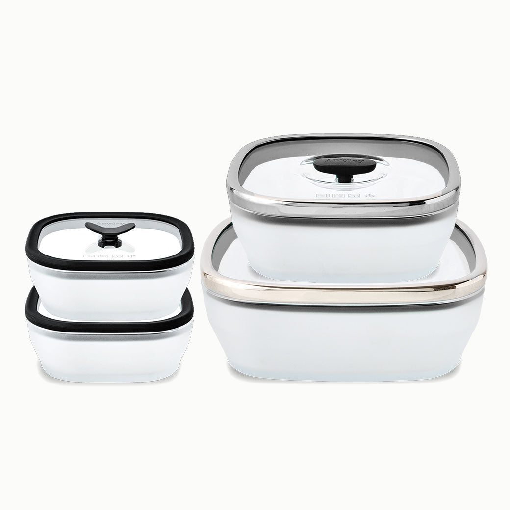 Four square frosted glass food storage containers from the Anyday 8-Piece Glass Square Dish Set in Black Sesame, each with a glass lid featuring a silicone rim and central handle, ideal for microwave cookware.