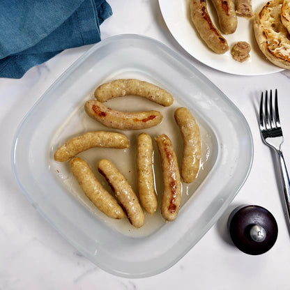 Cooked breakfast sausages in an Anyday dish, served next to a plate with a few sausages and an English muffin.