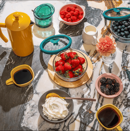 A vibrant breakfast spread featuring an Anyday Everything Dish filled with fresh strawberries, surrounded by an assortment of berries, coffee, and whipped cream. The plastic-free, airtight glass container provides sustainable food storage, keeping ingredients fresh and ready to serve. The Anyday Everything Dish is perfect for prepping, storing, and serving fruits, ensuring a stylish and functional addition to any kitchen.