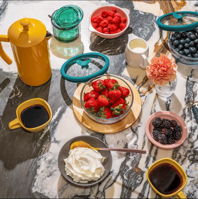A vibrant breakfast spread featuring an Anyday Everything Dish filled with fresh strawberries, surrounded by an assortment of berries, coffee, and whipped cream. The plastic-free, airtight glass container provides sustainable food storage, keeping ingredients fresh and ready to serve. The Anyday Everything Dish is perfect for prepping, storing, and serving fruits, ensuring a stylish and functional addition to any kitchen.