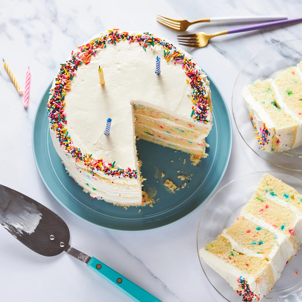 Festive birthday cake with spongy layers and homemade buttercream, served on a clear glass Anyday dish