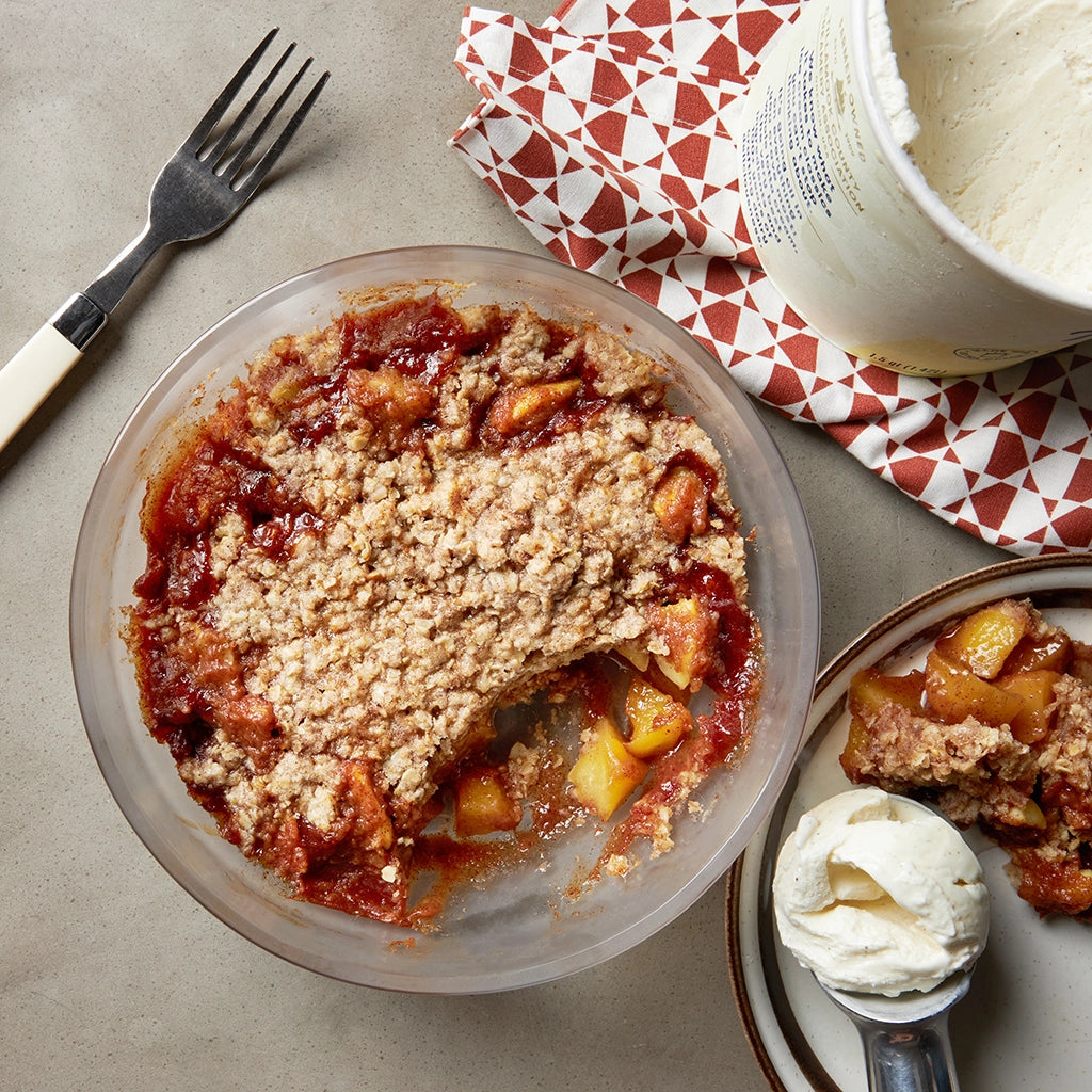 Apple crumble with a delicious oat topping served in a clear glass Anyday dish, accompanied by a scoop of vanilla ice cream.