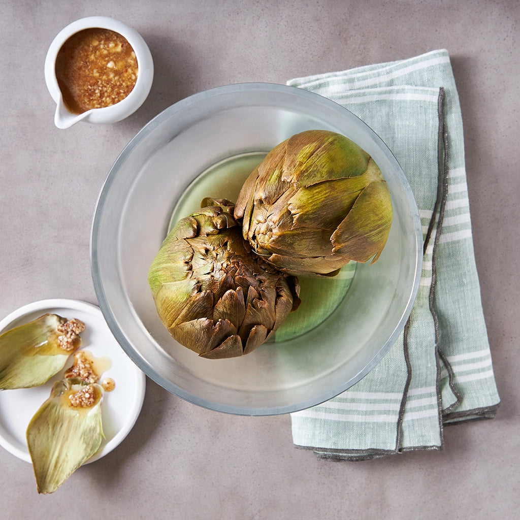 David Chang's steamed artichokes served in a clear glass Anyday dish, paired with a flavorful Bagna Cauda sauce.