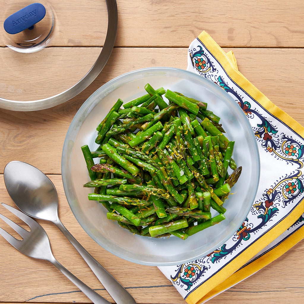 Asparagus with lemon butter served in a clear glass Anyday dish, showcasing bright green asparagus pieces coated in a zesty lemon butter sauce.