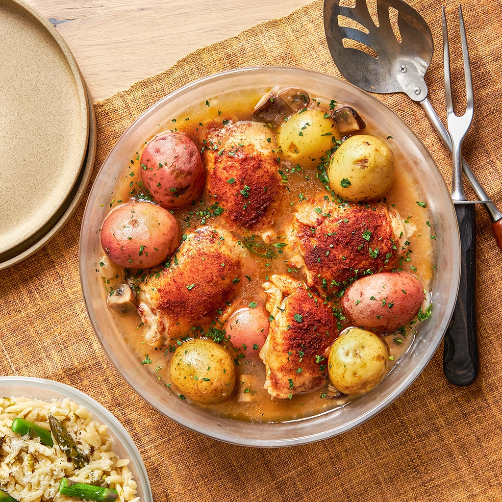 Beer-braised chicken with red and yellow potatoes made and served in a clear glass Anyday dish, garnished with fresh parsley.