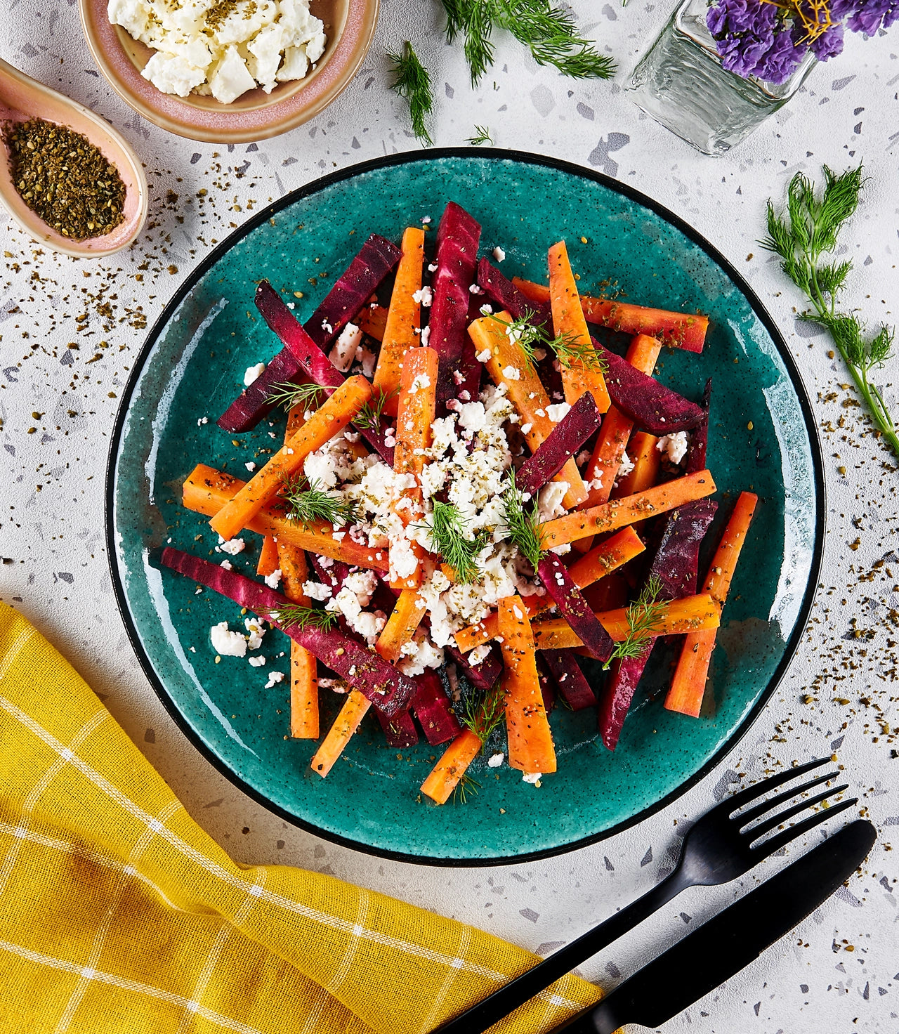 Beet and carrot salad with crumbled feta cheese, garnished with fresh dill, made in a glass Anyday dish and served on a green plate.