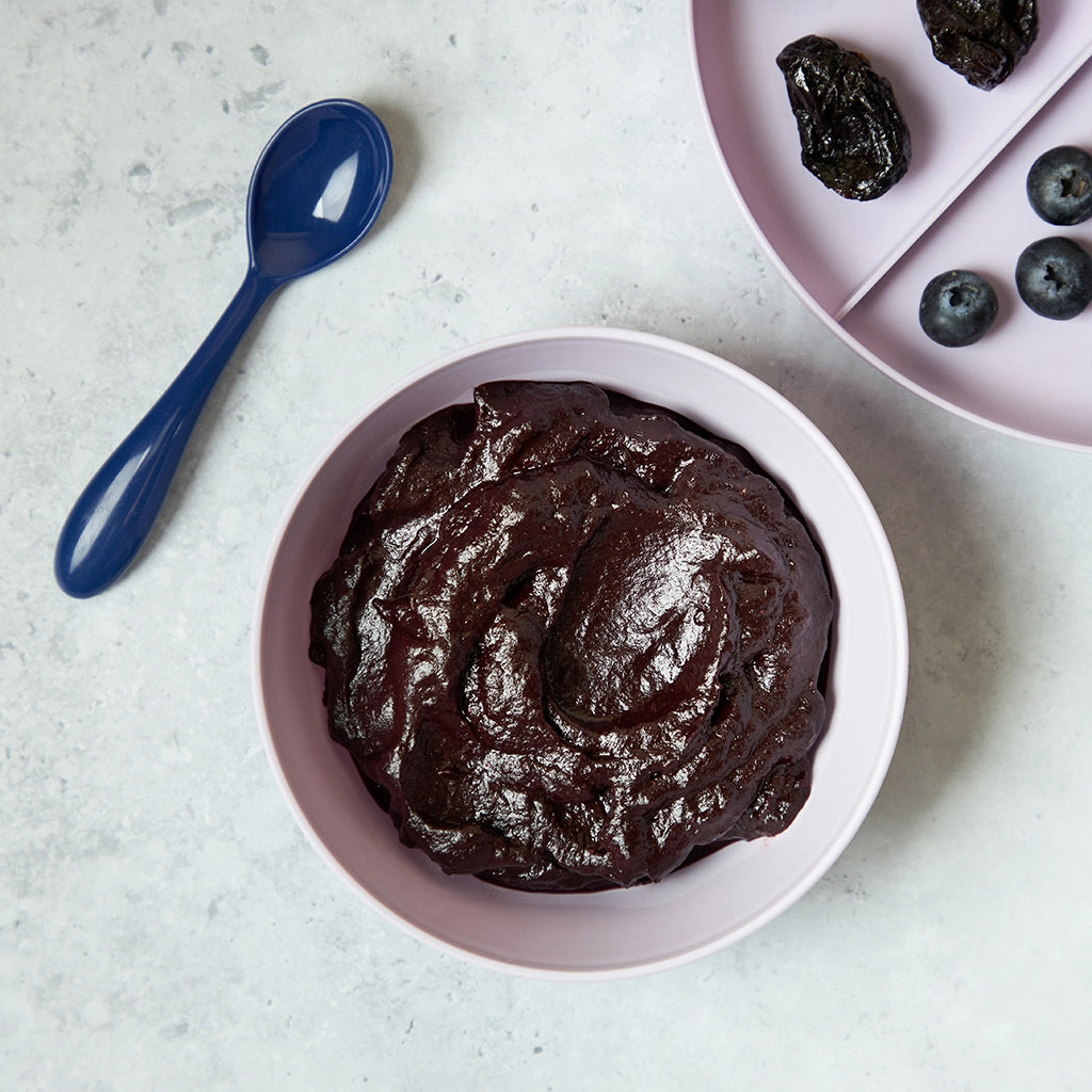 Blueberry prune puree made in a glass Anyday dish served in a pink bowl with a blue spoon on the side, great for babies.