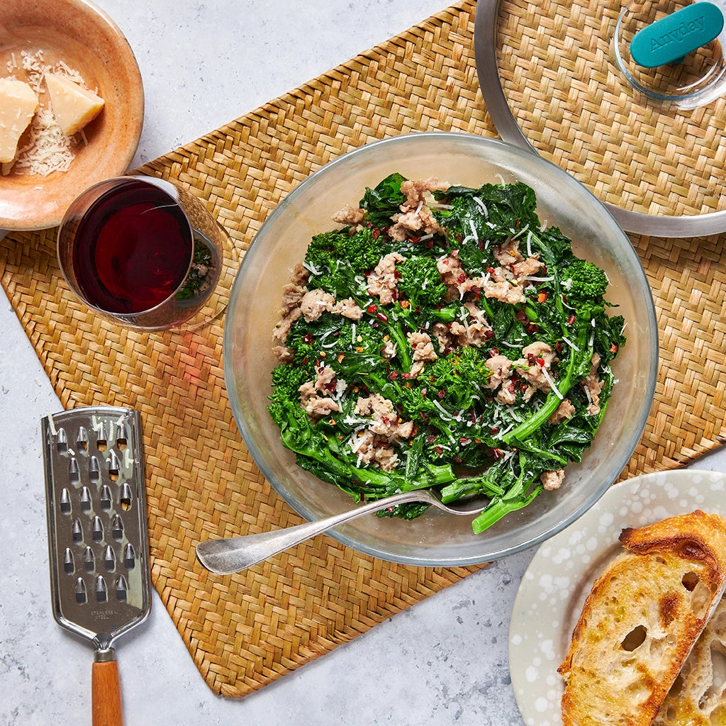 Broccoli rabe with sausage and parmesan, made and served in a clear glass Anyday dish, garnished with grated cheese and red pepper flakes.