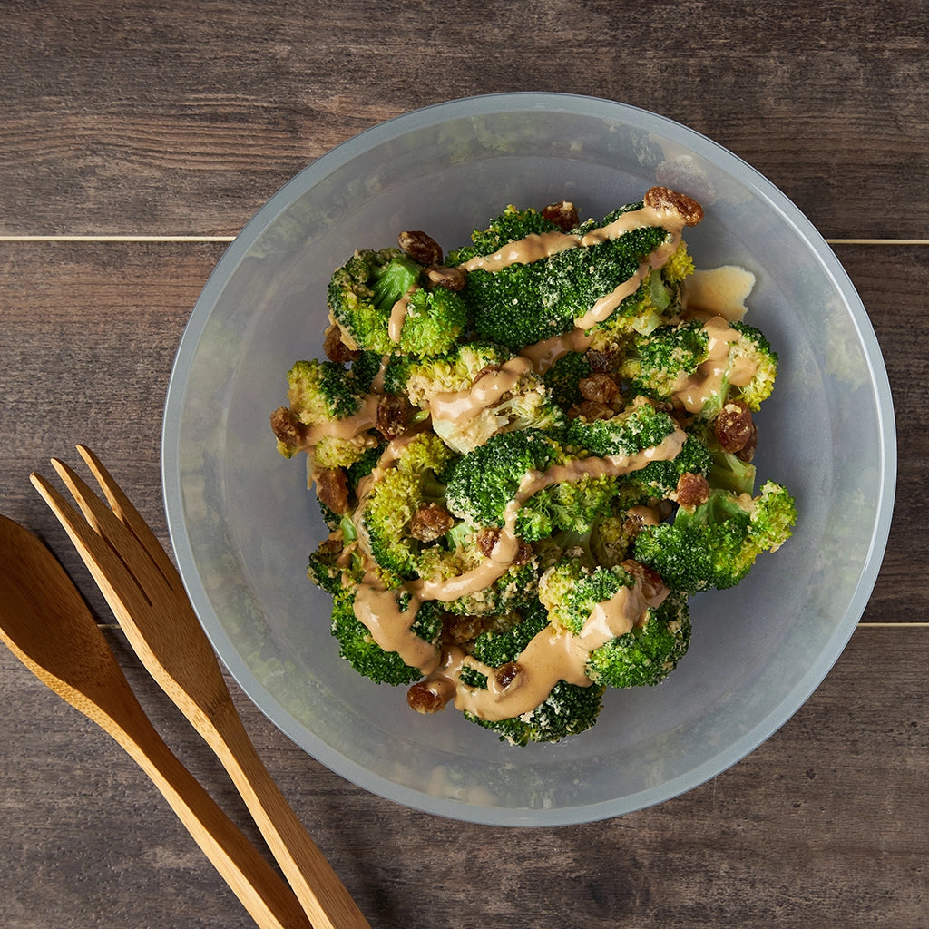 Broccoli with tahini sauce and golden raisins, made and served in a clear glass Anyday dish, garnished with sesame seeds.