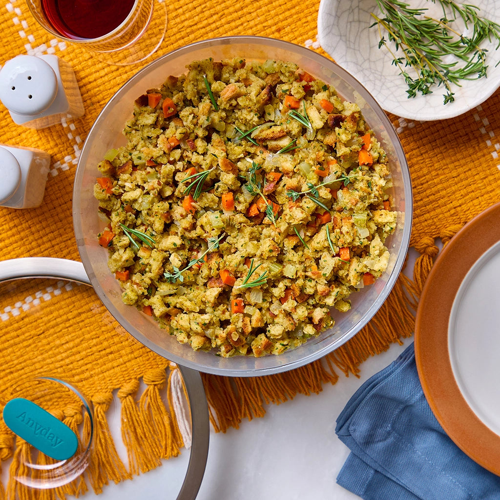 Brown butter stuffing with carrots and celery made in a glass Anyday dish, garnished with fresh rosemary, served in a clear glass Anyday dish on a yellow placemat.