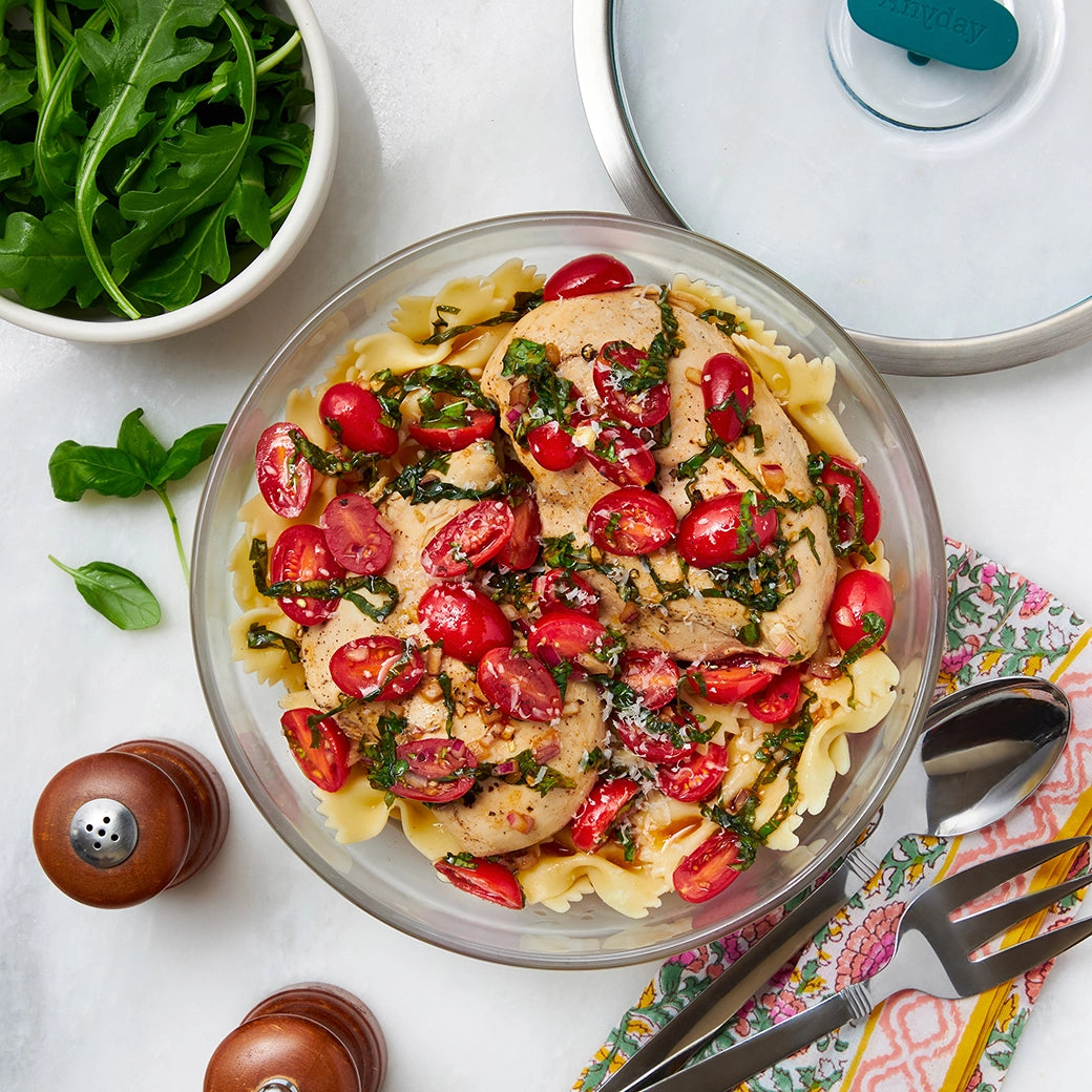 Bruschetta chicken pasta with tomatoes, basil, and grilled chicken, made and served in a clear glass Anyday dish.