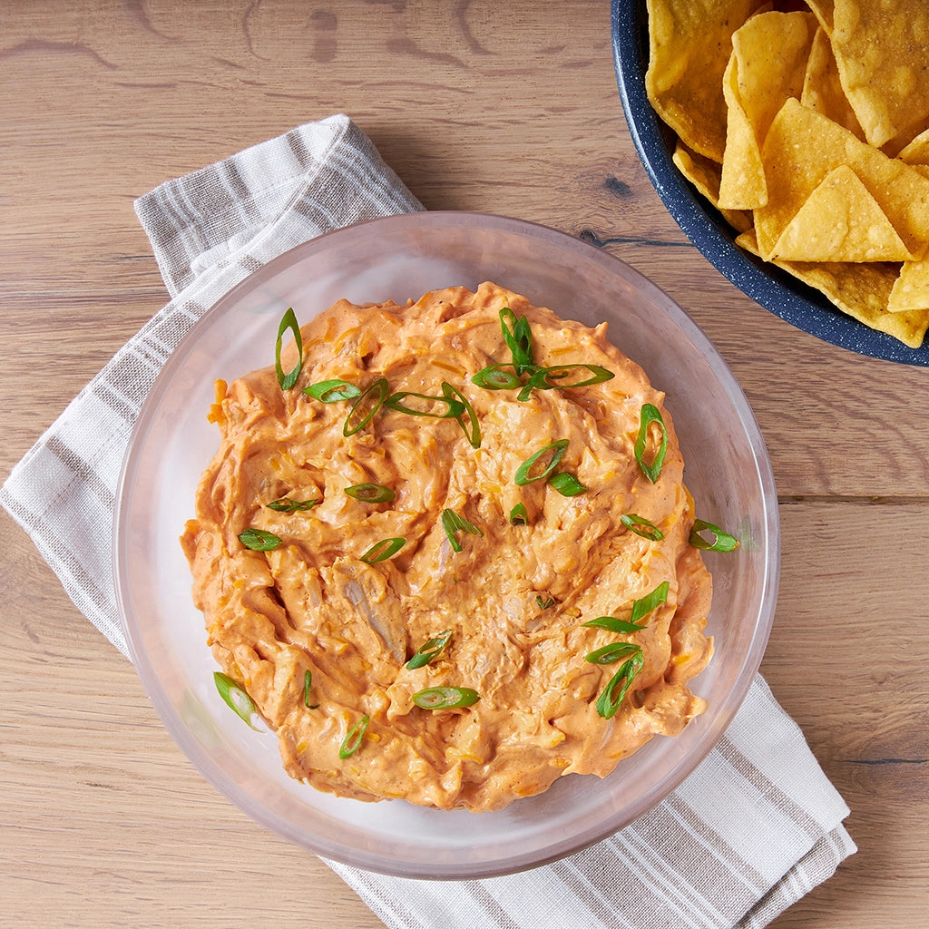 Buffalo chicken dip topped with melted cheese, made and served in a clear glass Anyday dish, with celery sticks and crackers on the side.