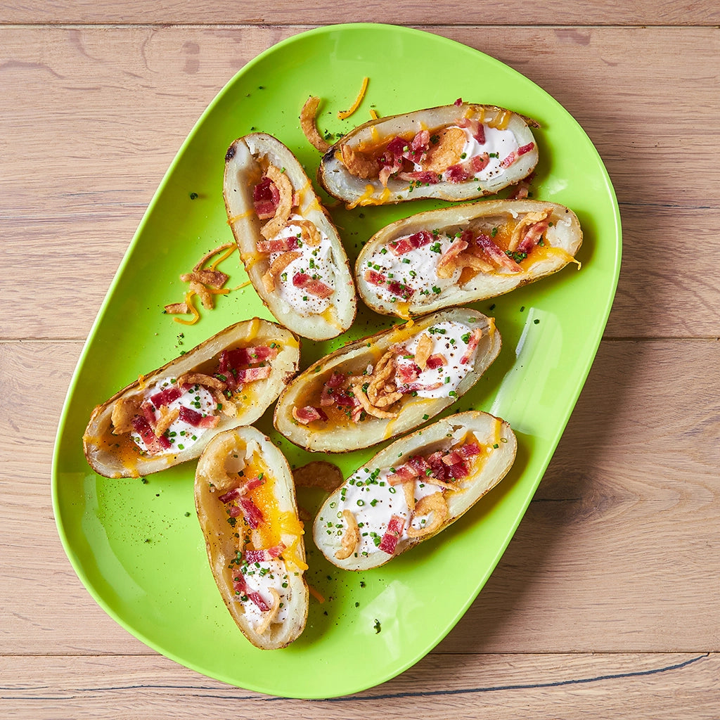 Flavorful microwave-loaded potato skins in a glass Anyday dish, consisting of crispy shells topped with cheese, bacon bits, and green onions for a quick snack.