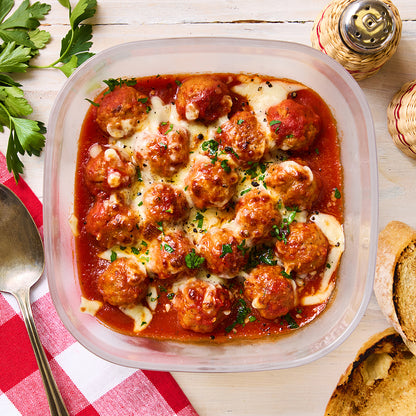 Microwave-cooked meatballs in marinara sauce, topped with melted mozzarella and chopped parsley, served in a glass Anyday dish next to crusty bread and a red-checked napkin.