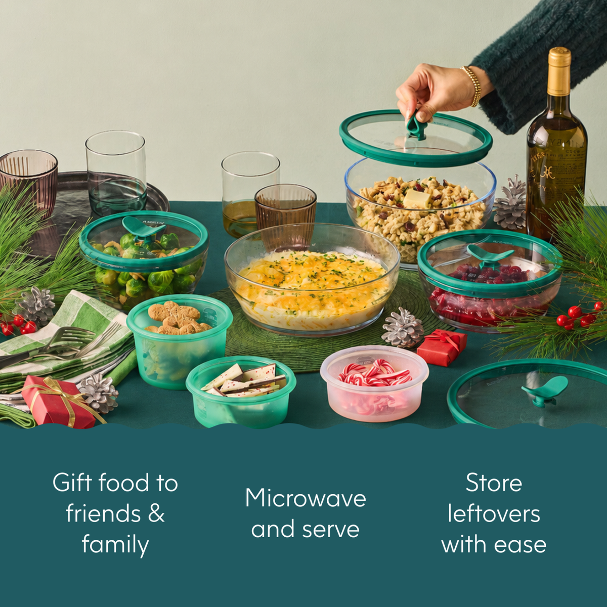 A hand places a lid on an Anyday The Everything but the Microwave Bundle dish filled with food, part of a set arranged among glass and silicone containers on a holiday-themed table.