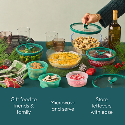A hand places a lid on an Anyday The Everything but the Microwave Bundle dish filled with food, part of a set arranged among glass and silicone containers on a holiday-themed table.