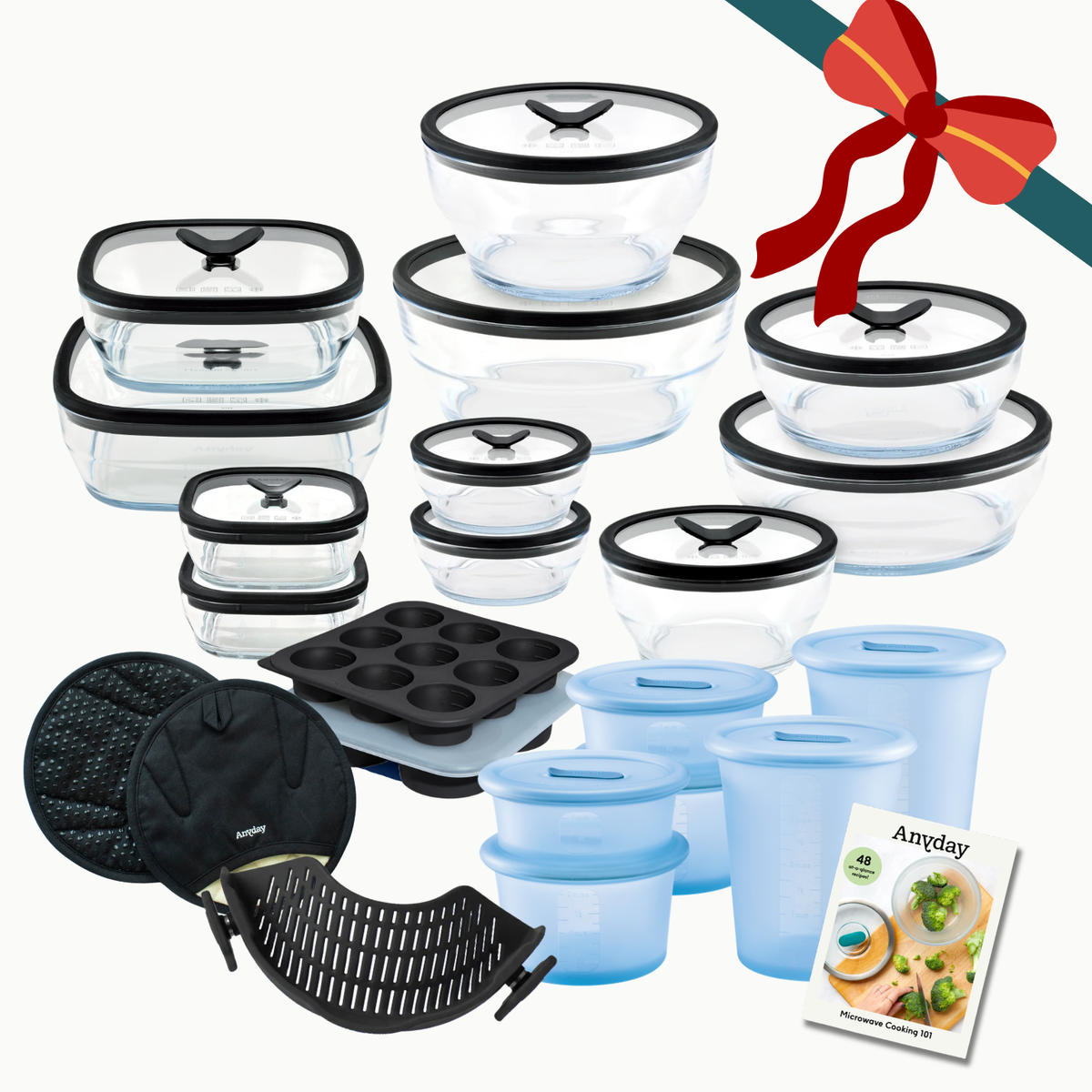 The Everything but the Microwave Bundle (black) featuring glass dishes with black lids, blue silicone containers, a muffin tin, black mitts, a steaming tray, and a recipe booklet, all tied with a decorative red bow.