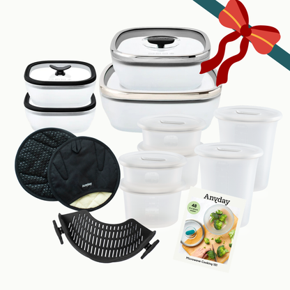 The Ultimate Gift Bundle (black) featuring glass dishes with lids, silicone containers, two oven mitts, a silicone steamer insert, and a microwave cooking recipe book, all tied with a decorative ribbon.