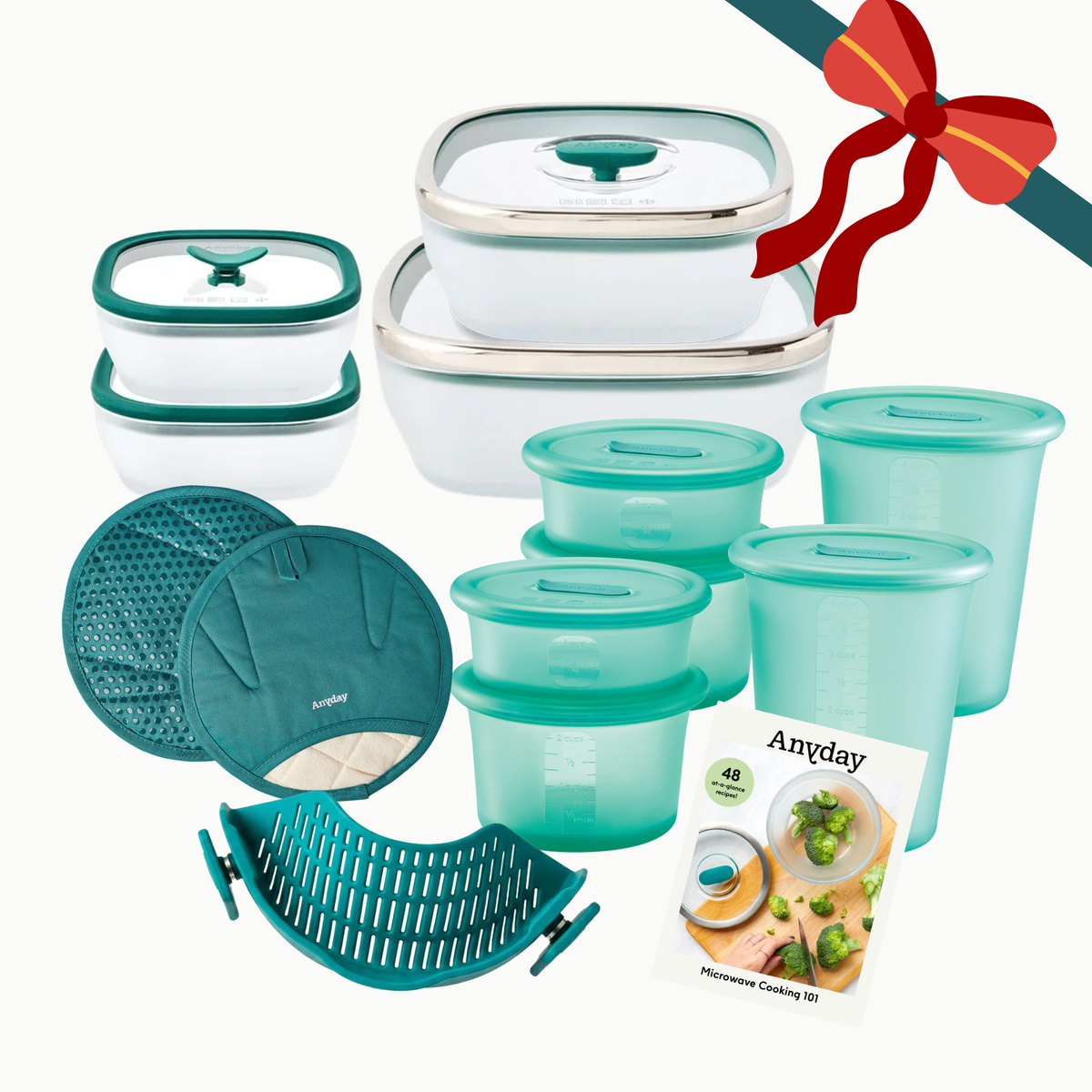 The Ultimate Gift Bundle (kale) kitchen essentials set featuring glass dishes with glass lids, silicone containers, a steamer basket, two pot holders, and a microwave cooking guide, tied with a decorative red ribbon.