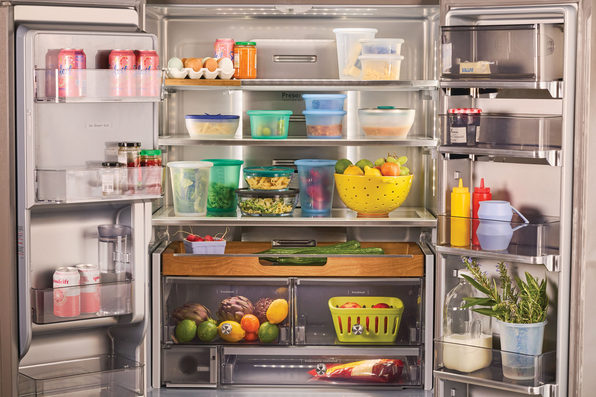 An open fridge filled with various foods in containers, bottles, fruits, vegetables, and drinks. Eggs and sodas are on the top shelves, and produce is organized in the drawers and door compartments.